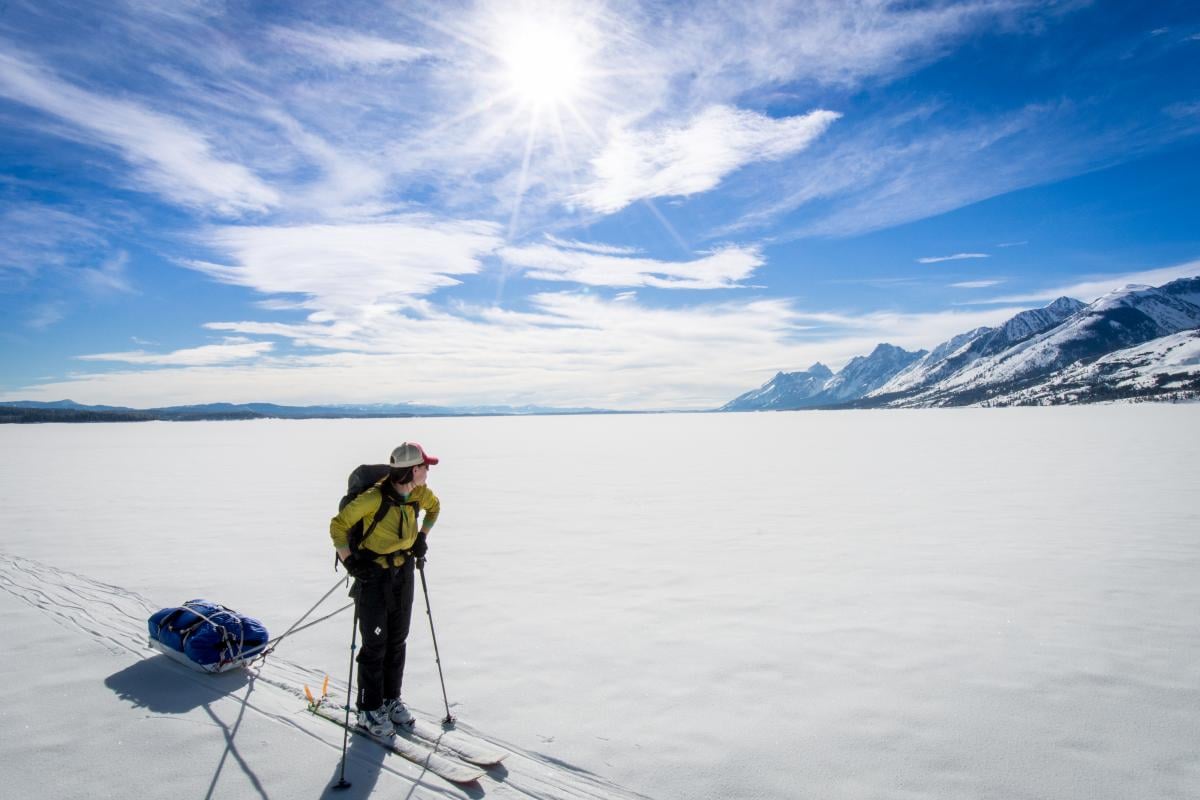 NOLS participant pulling sled looks out across a snowfield to distant mountains while backcountry touring