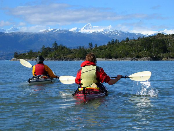 Students sea kayaking through Patagonia gaze at snow capped mountains in the distance. 