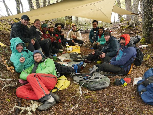 Smiling course participants gather together under a rain tarp for a meal in Patagonia. 
