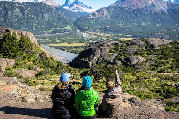 Several students sitting high up on a hill point to snow-capped peaks off in the distance in Patagonia.