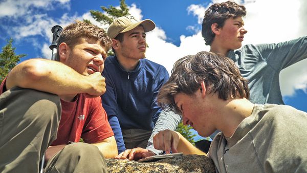 Four students look around at their surroundings and consult a map on an adventure course in the Adirondacks.