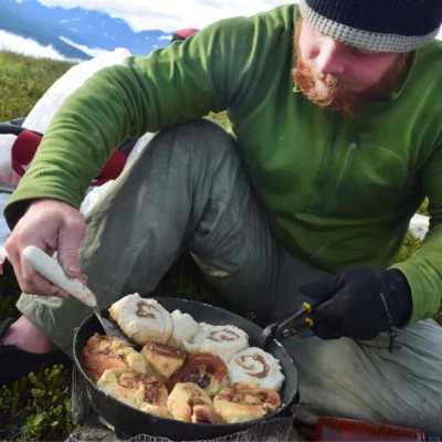 A student flipping some buttery, crispy, chewy cinnamon rolls on the last morning of backpacking in the Chugach Range.