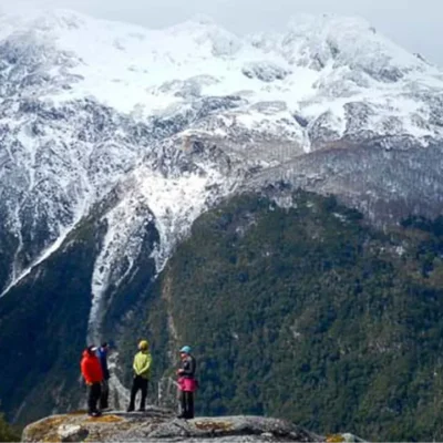 Four students pause on a rocky outcrop to admire a sweeping view of snow-capped peaks while mountaineering through Patagonia's Engano Valley.