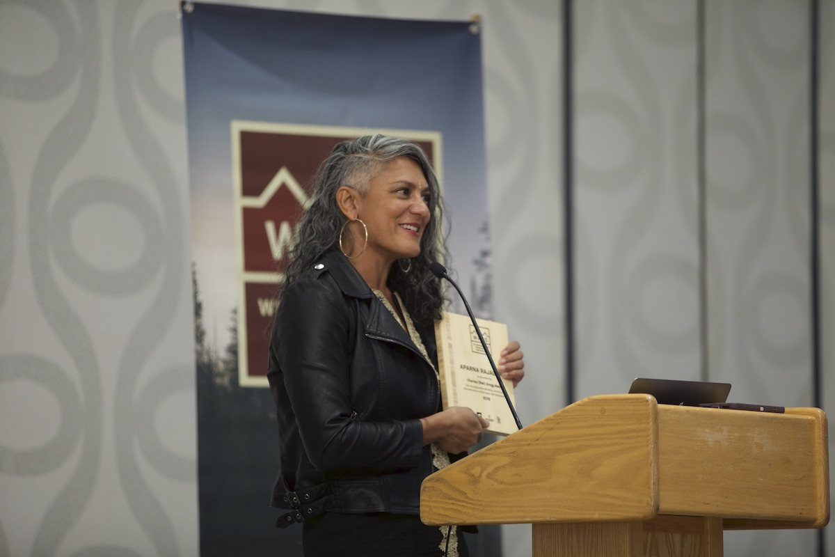 Aparna Rajagopal stands at wooden podium at the WRMC holding Reb Gregg award plaque