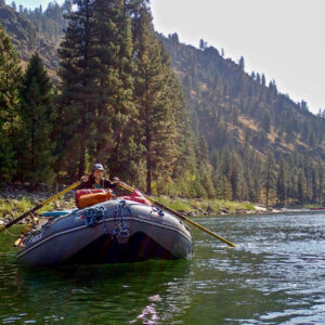 Teen girl with a big smile on her face on a raft solo holding the oars floating down river