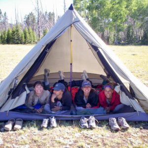 four teen girls racing the tent opening laying down looking at the camera with their shoes outside on the ground in front of them.