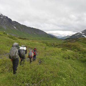 a few students backpacking through a lush green grassy area