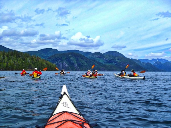 NOLS students sea kayaking in New Zealand with lush green mountains ahead, as viewed from a kayak