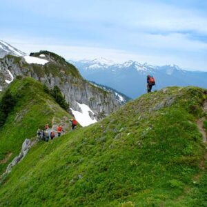 Students backpacking on scenic green hills amidst the snowy peaks of the North Cascades.