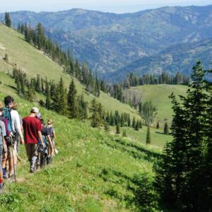 Small group of students hiking a single track through a green wilderness wearing t shirts and shorts.