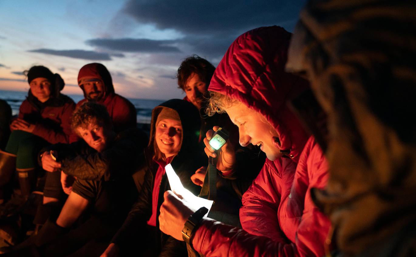 oscar_manyguy_pat-68.jpg__1370x846_q70_crop_subject_location-1166,653_subsampling-2 A student uses a headlamp to read off a piece of paper during a group meeting around the campfire.