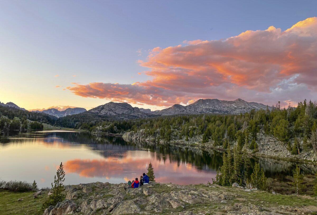Purple clouds over granite peaks. There's a lake reflecting the clouds in the foreground.