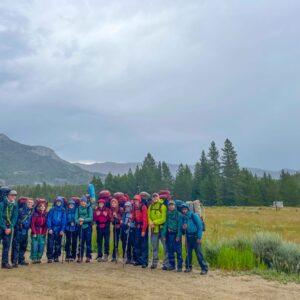 Group of teens wearing rain gear with a cloudy sky standing on a flat dirt trail