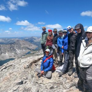 Group of teens standing on top of a large rock at elevation with mountains off in the background