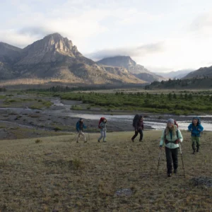 five backpackers hikeup a grassy hill. there are tall granite peaks in the background.