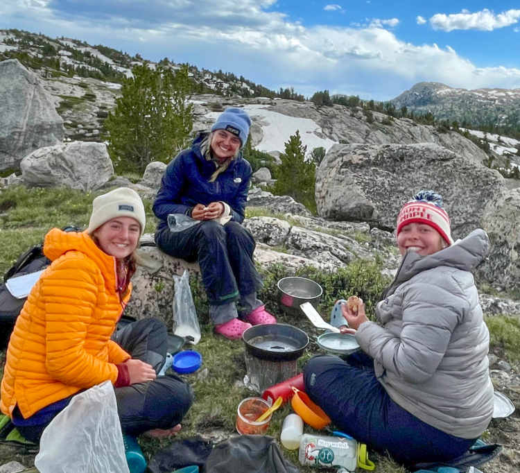 Three young women sitting on rocks, eating.