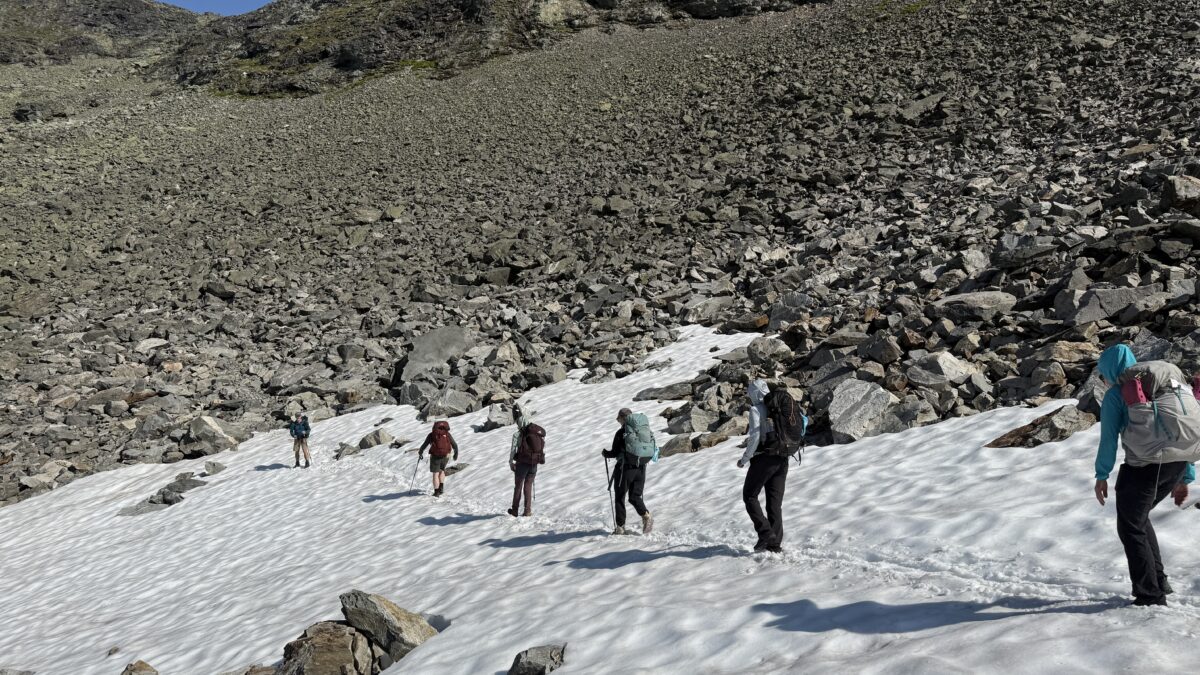 Six hikers travel single file down a snow-covered rocky mountainside.