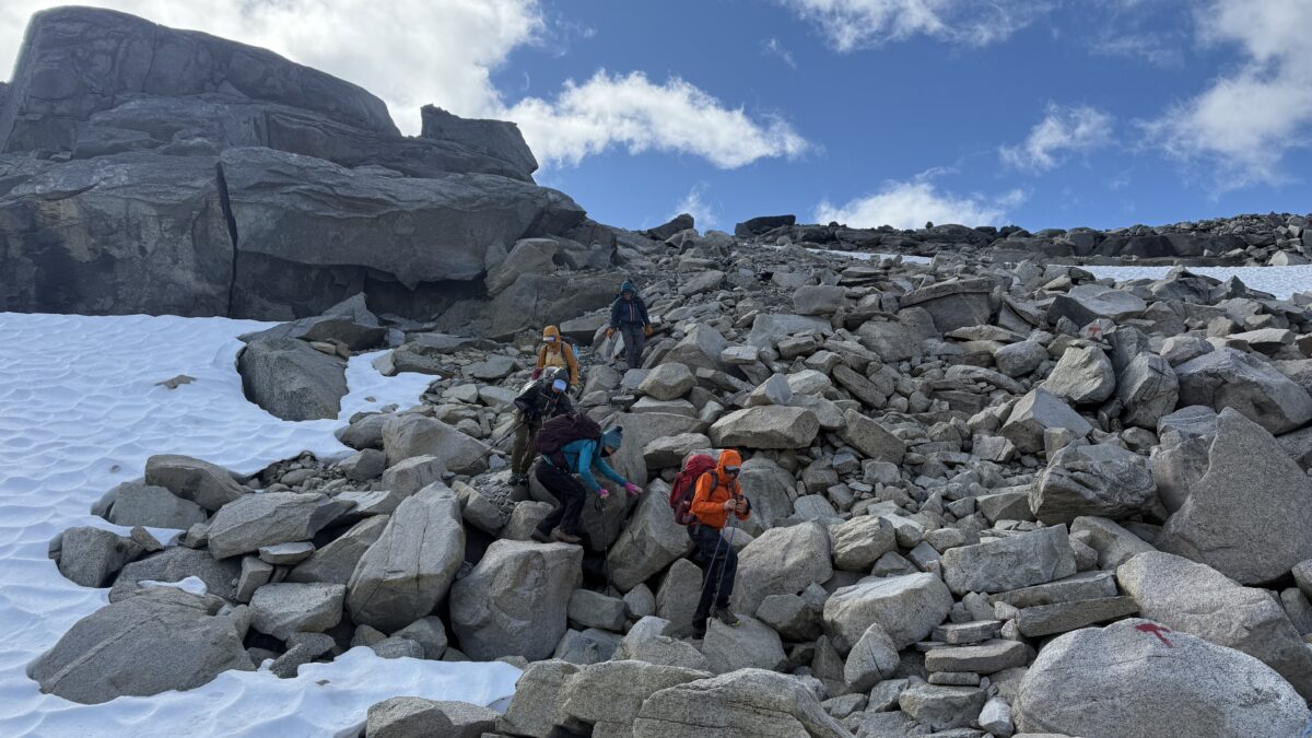 Group in colorful outerwear carefully moves over very rocky terrain; blue sky in background.