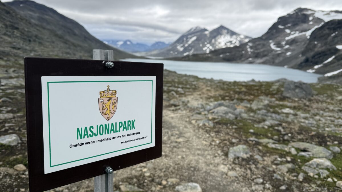 Sign for national park with mountains and lake in background.