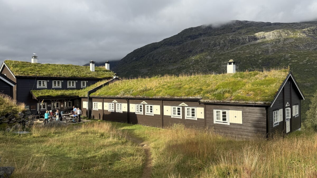 Sod-roofed building with group of 5-6 people on a patio prepping for a meal.