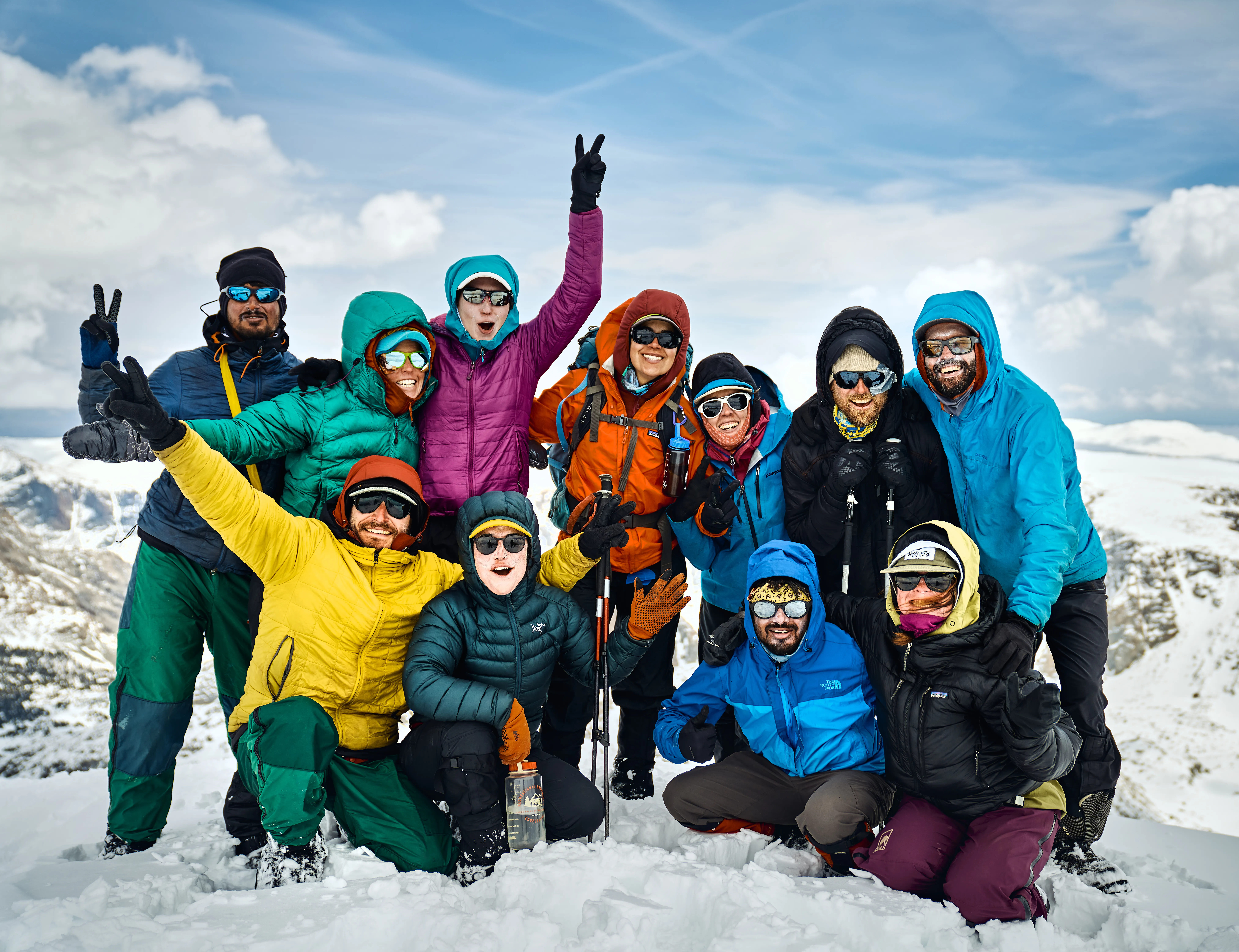 A group of people dressed for the cold stand on snow. They are posing as a group and smiling at the camera.