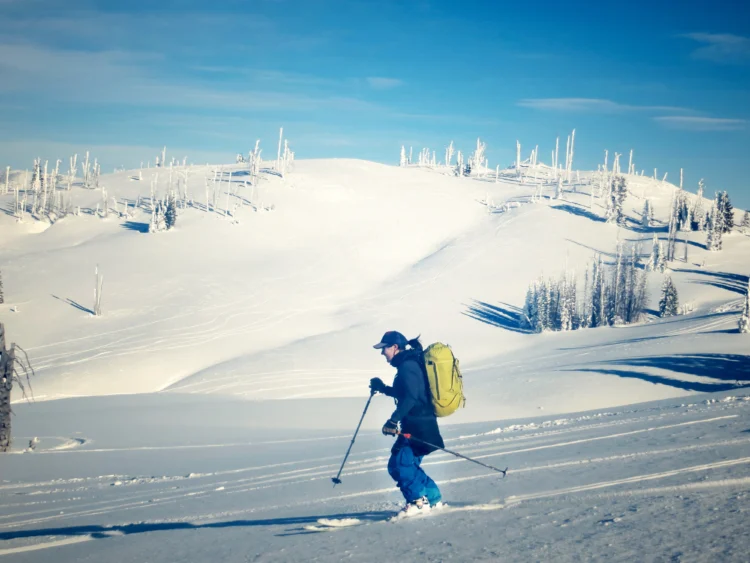 a female skier cruises on a mellow slope. There are snowy hills in the background.