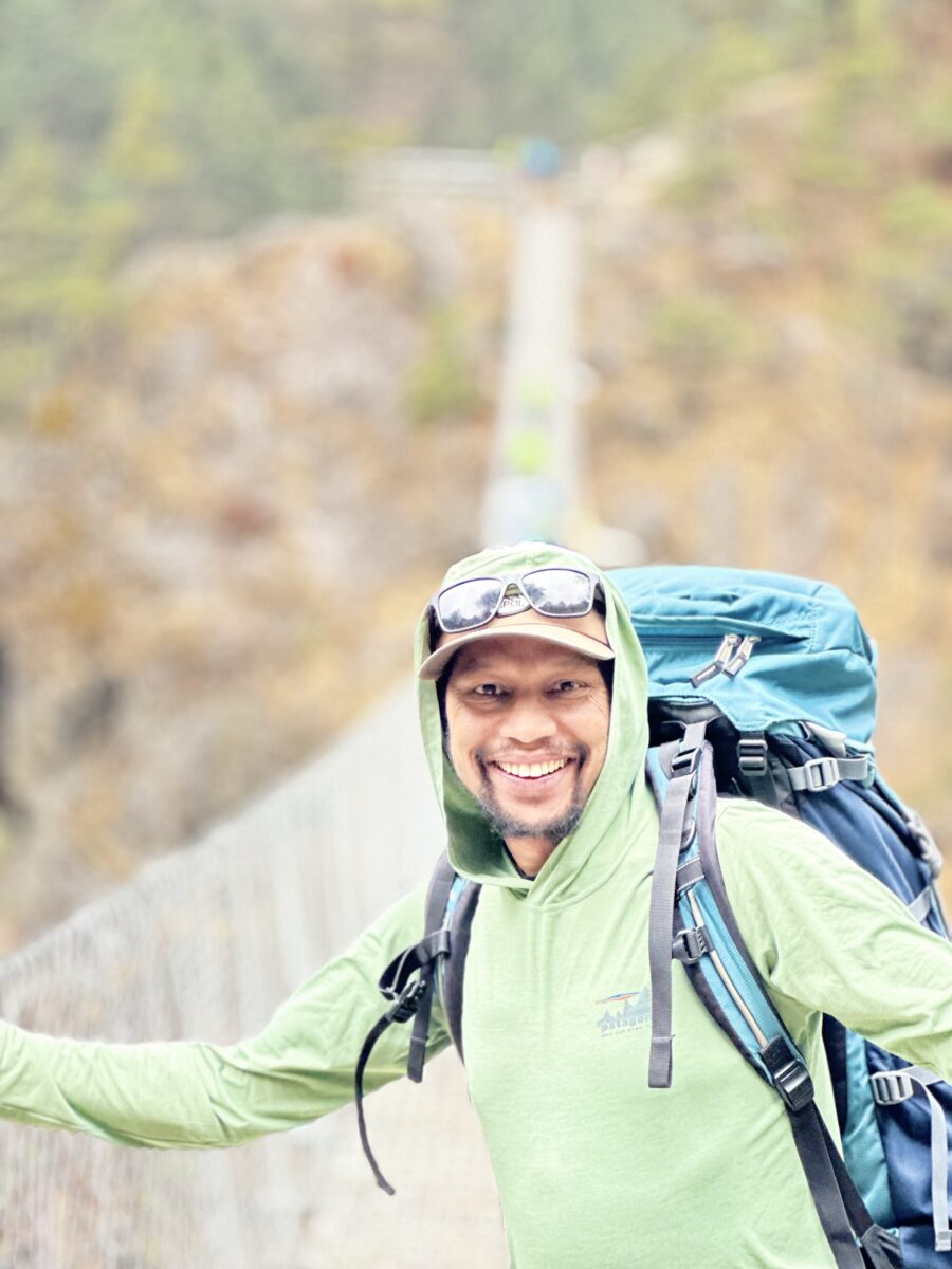 Jagan Timilsina, wearing a light green jacket and a blue backpack,  photographed on a bridge.