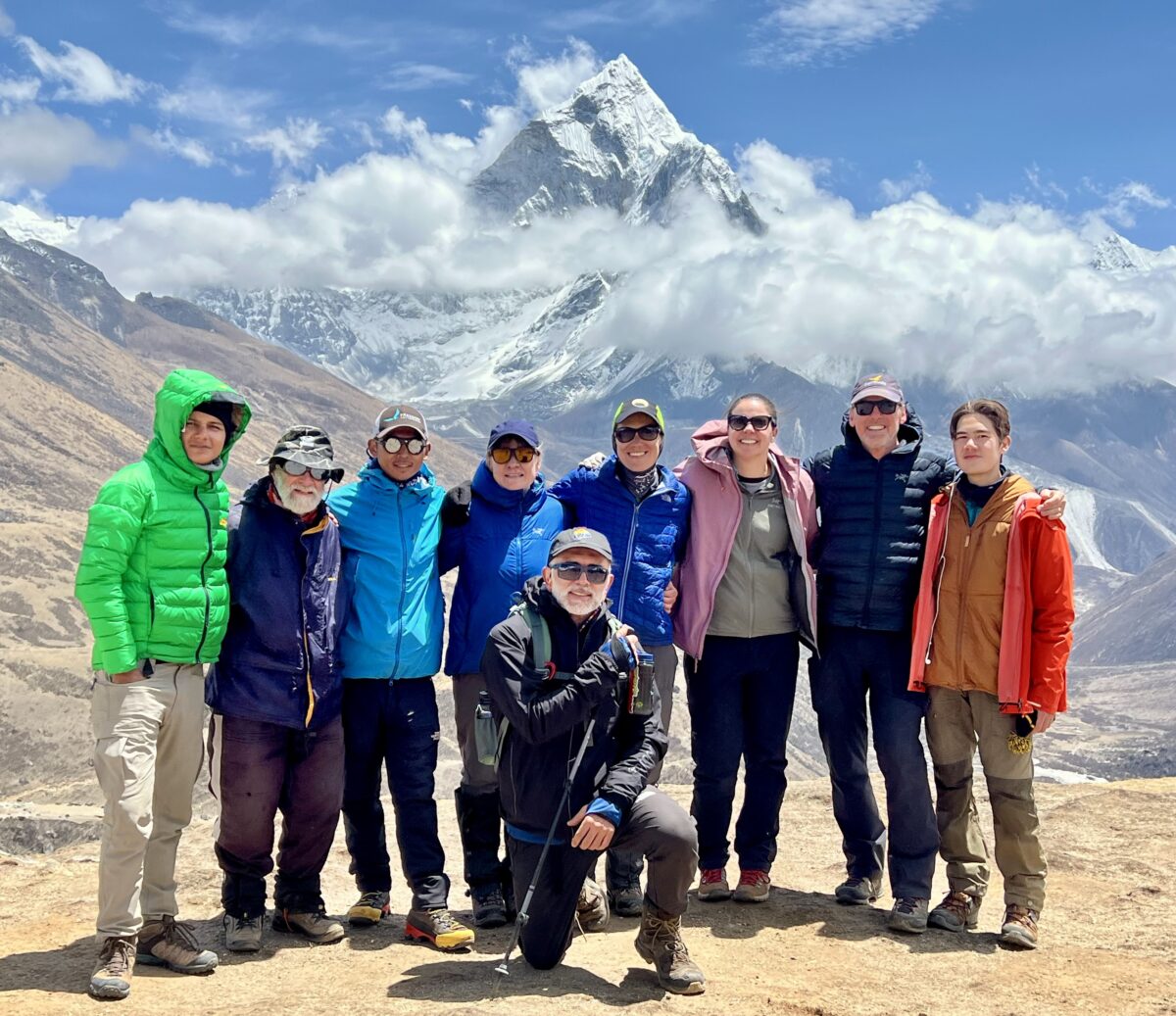 Team members, in brightly colored jackets, pose together with Everest in the distance.