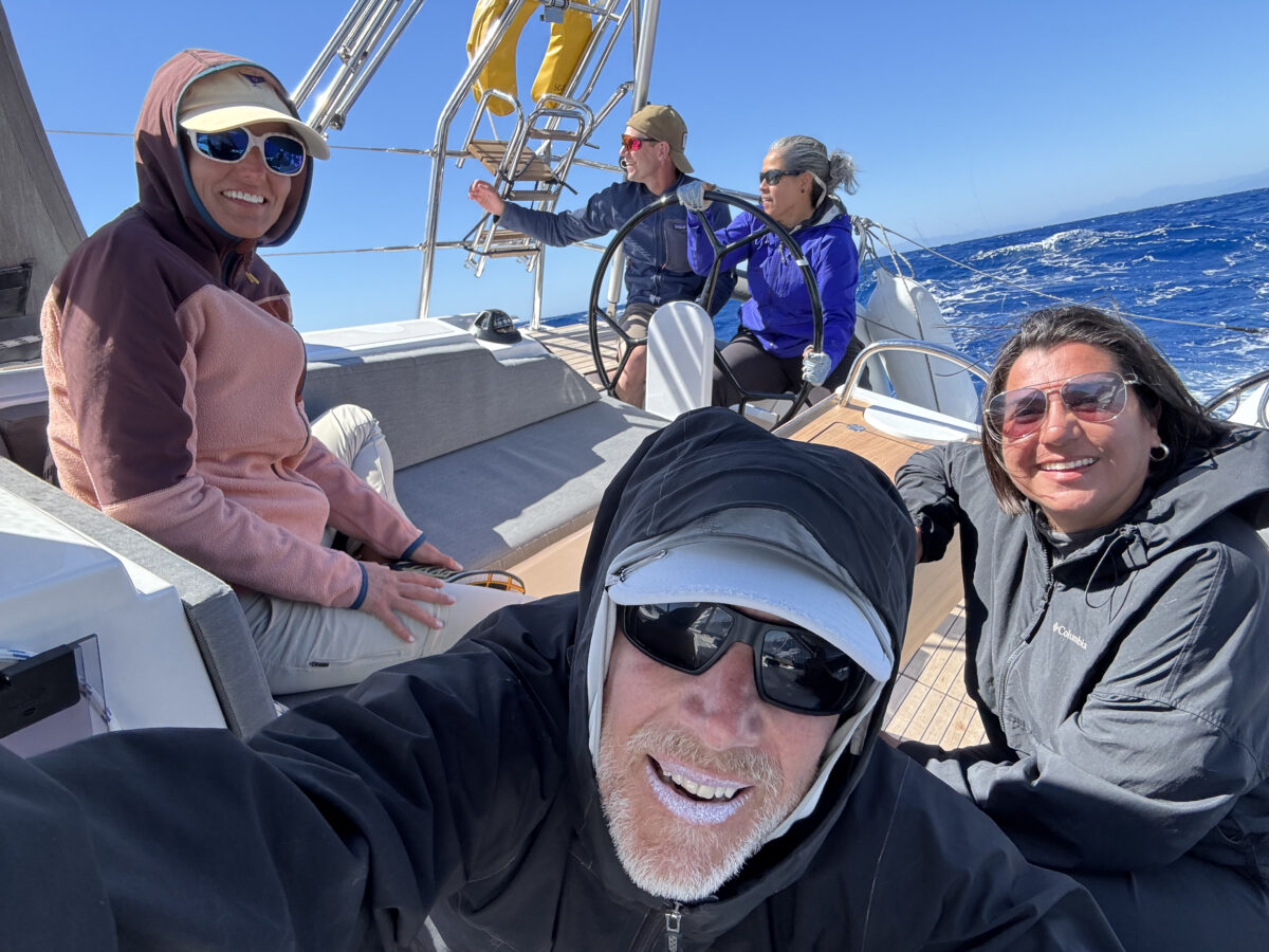 Five crew members sit on the deck on mildly choppy sea. 