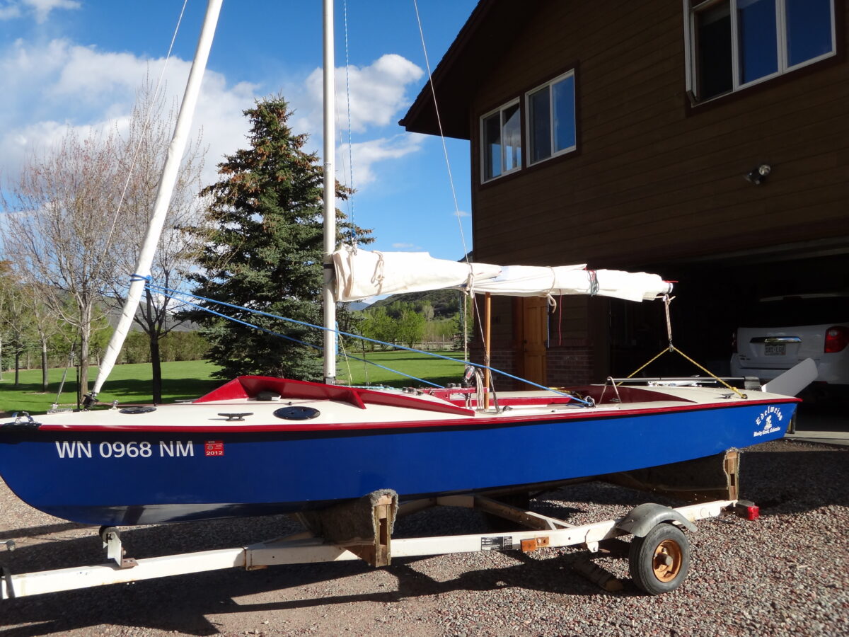 A red, white, and blue 16-foot racing dinghy, called a Snipe, that Nick built,sitting outside his childhood garage.