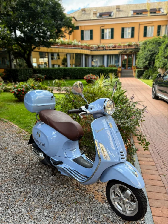 Light blue moped is parked in front of a charming yellow hotel.