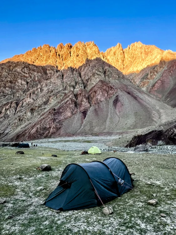 Tents stand before towering cliffs with alpenglow turning the cliffs golden yellow