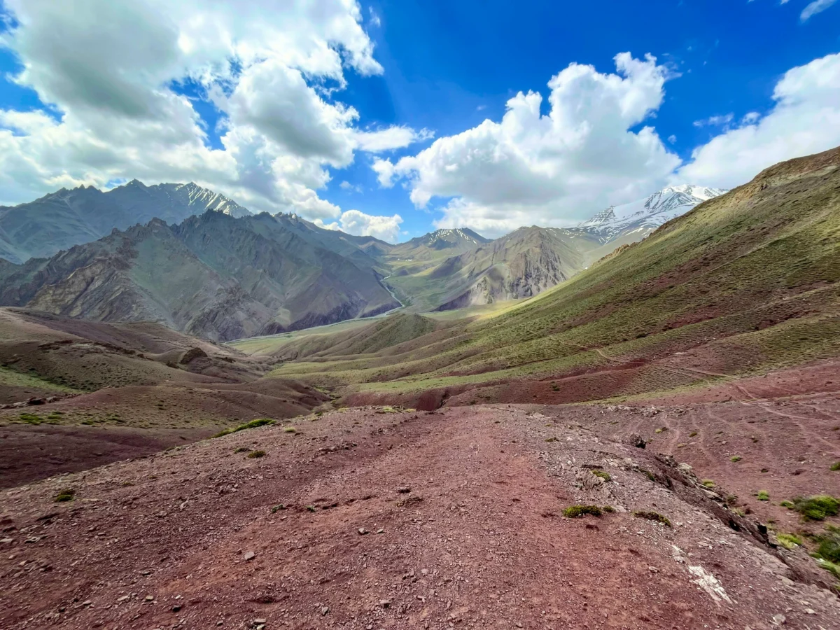 The trail points towards towering peaks, cloud, and sun in the distance.
