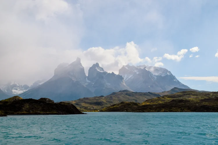 Steep peaks shrouded in mist with turquoise water in the foreground.