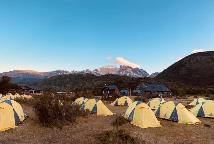 mountaineering tents lined up in a field. There are mountains in the background.