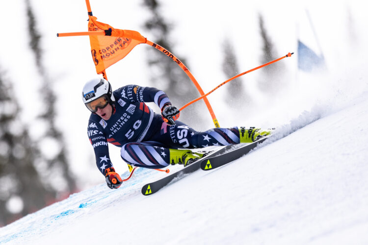 A male skier in a blue ski suit takes a tight turn on a steep mountain