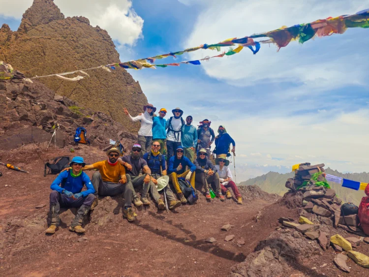 The hikers pose at the top of a pass with prayer flags blowing in the wind.