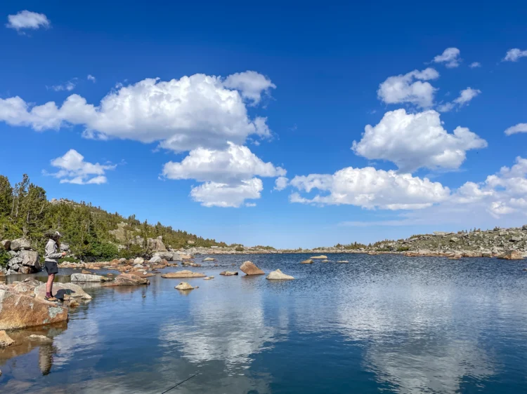 A person fishes in an alpine lake.