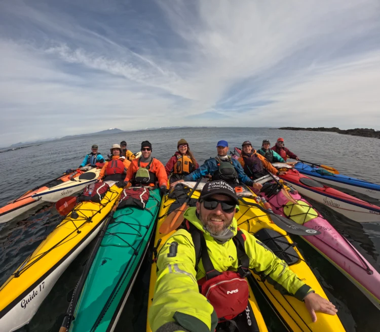 A group of people in brightly colored sea kayaks clumps together for a selfie on the ocean. 