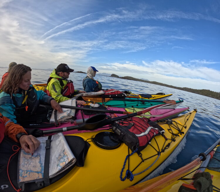 Kayakers look at the map with their kayaks pulled up together in the sea