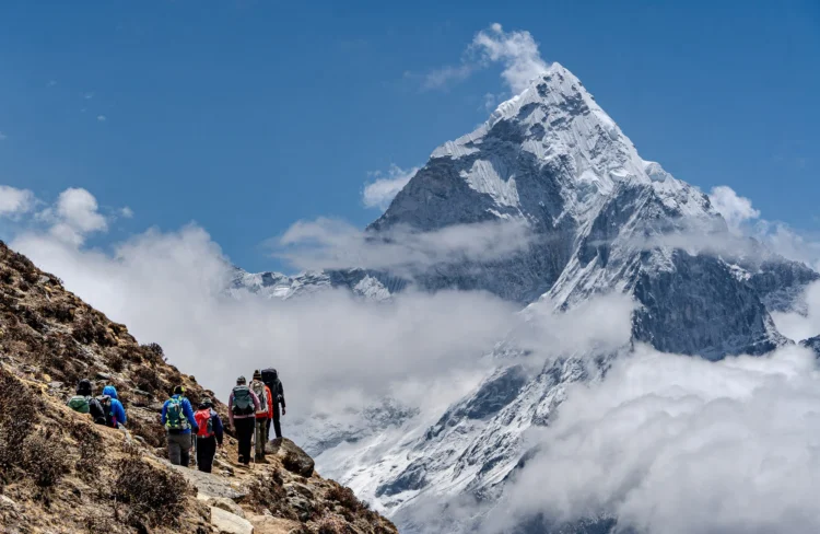 Hikers walk on the trail with towering Himalayan peaks in the distance