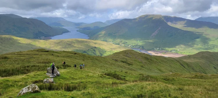 Hikers walk through green fields towards the mountains