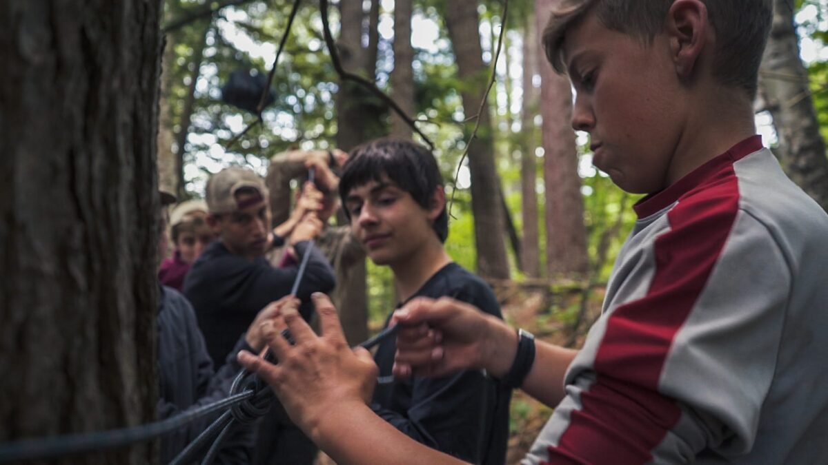 Teens working together on a rope activity in a forest during a nature-based therapy program.