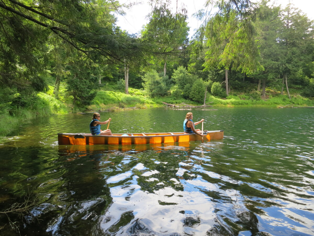 Two women paddling a canoe on a serene body of water.