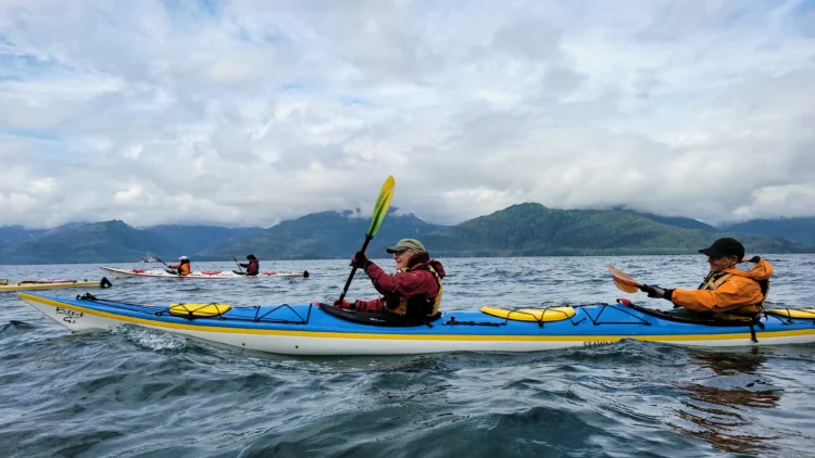 Kayakers paddle in Prince William Sound with mountains in the background