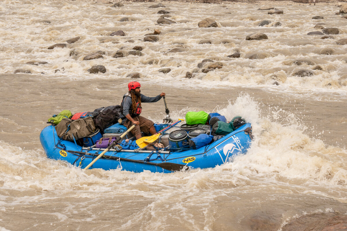 a man in a red helmet steers a blue raft through a whitewater rapid