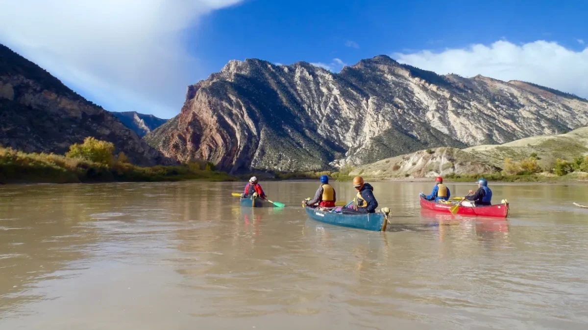 a group of people in canoes paddle down a muddy river. there are large red mountains in the background