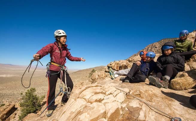 Students sitting on a rock ledge listen to an instructor's climbing lesson in the northern Rockies.