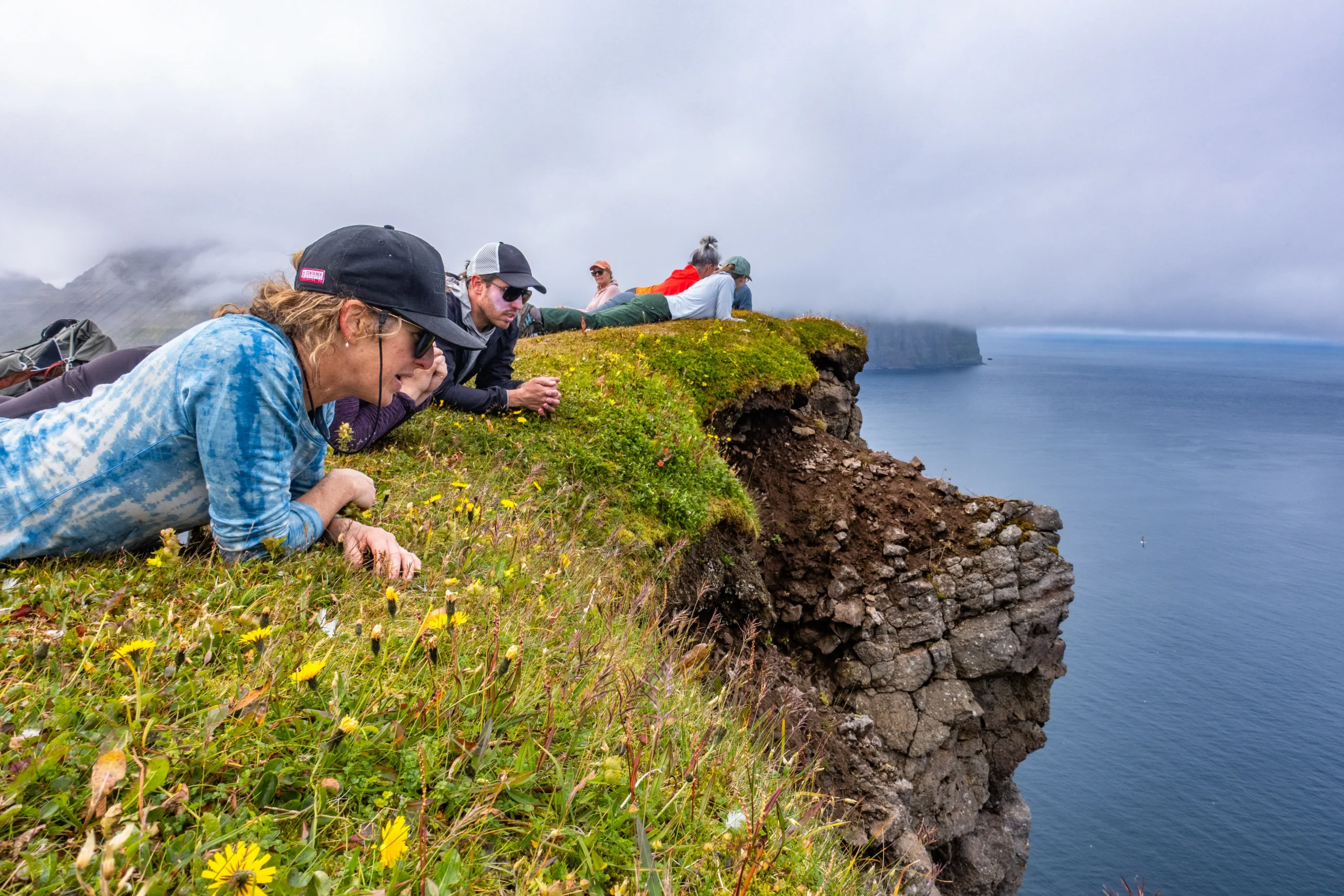 Hikers look over a cliff into the sea in the Westfjords