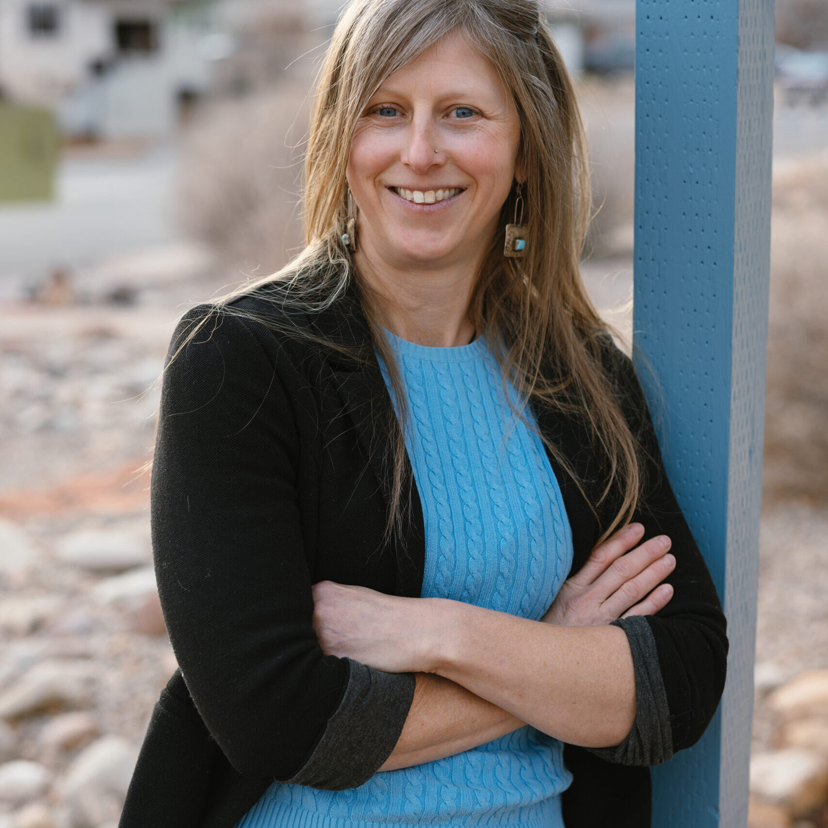 A woman with blonde hair and a blue shirt leans against a blue girter.